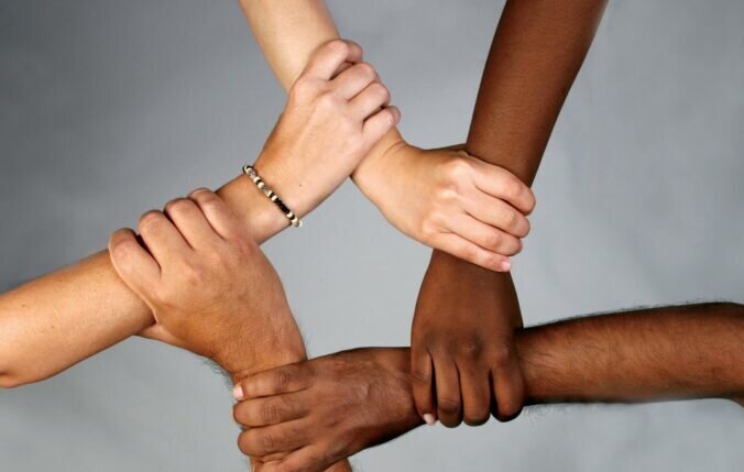 Four hands of different skin tones reaching out to each other