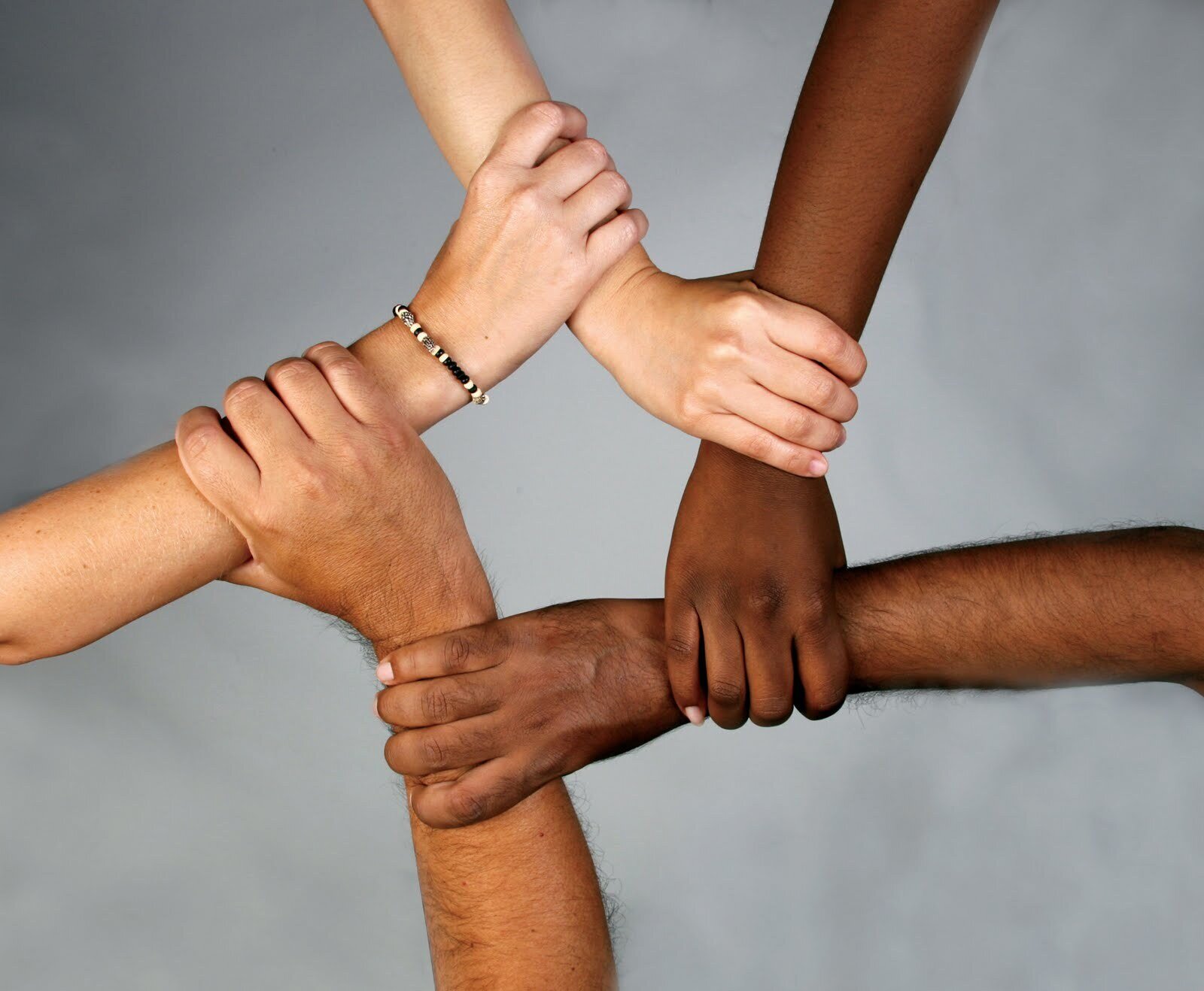 Four hands of different skin tones reaching out to each other