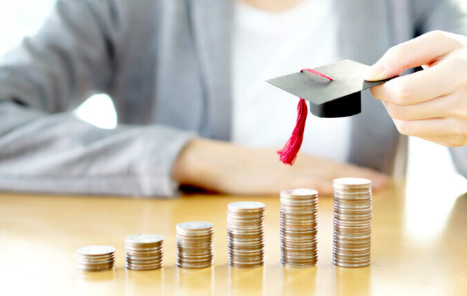 A person holding a mortarboard above stacks of coins