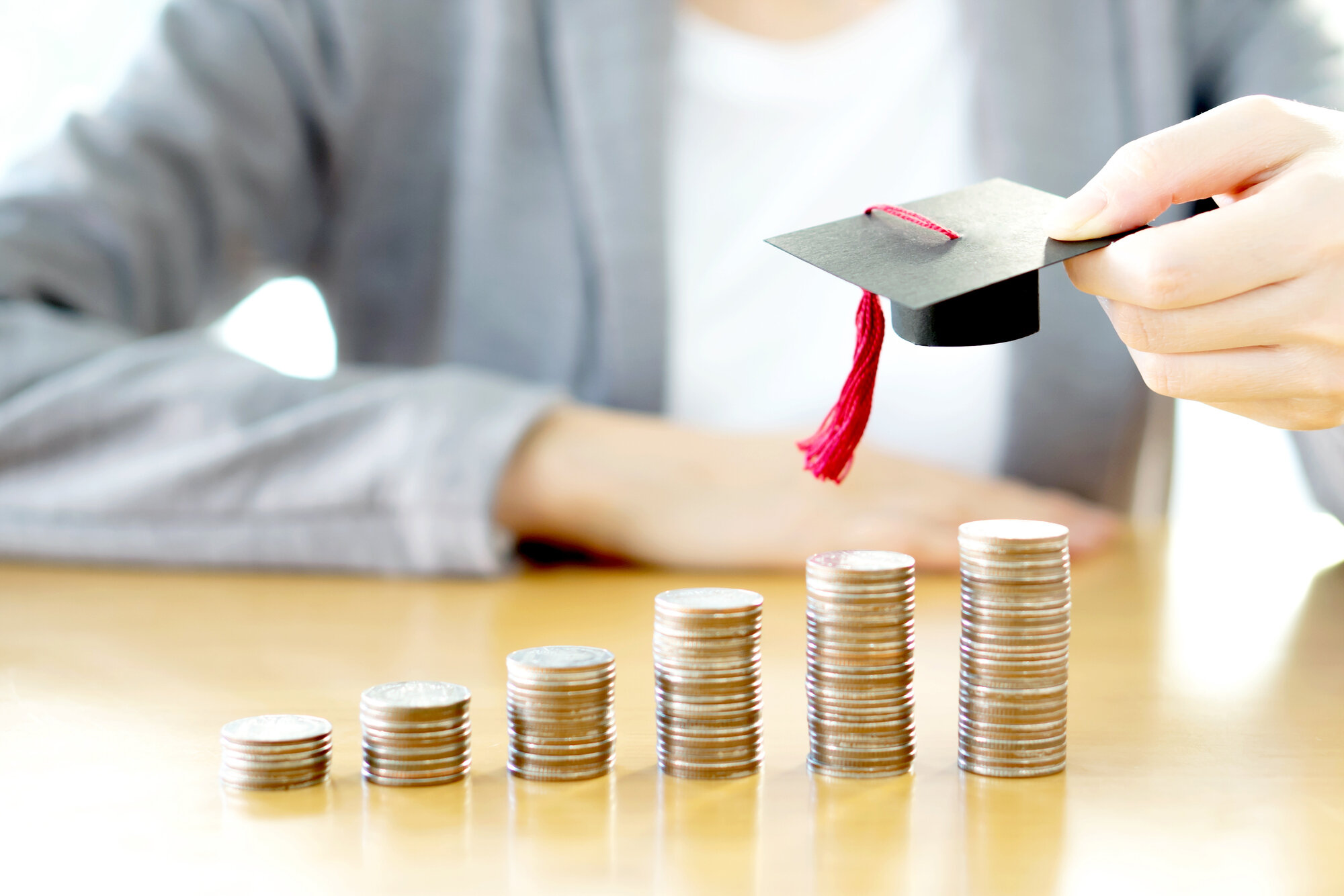 A person holding a mortarboard above stacks of coins