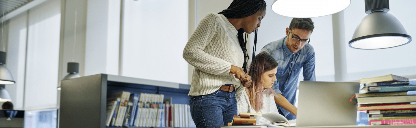 A woman standing up and looking at the work her seated colleague is doing