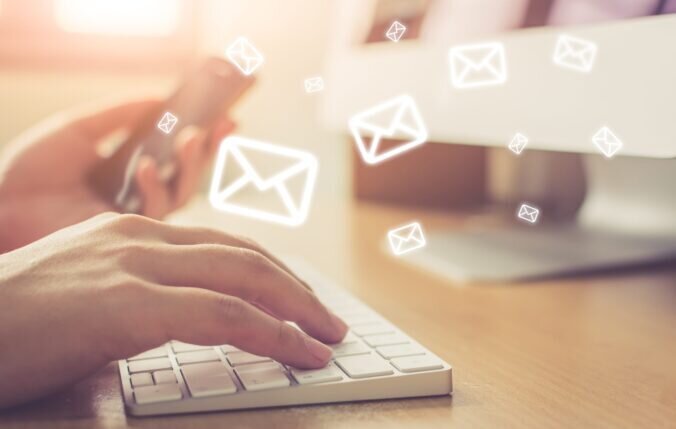 Close-up of hands typing on a keyboard with graphics of envelopes surrounding them