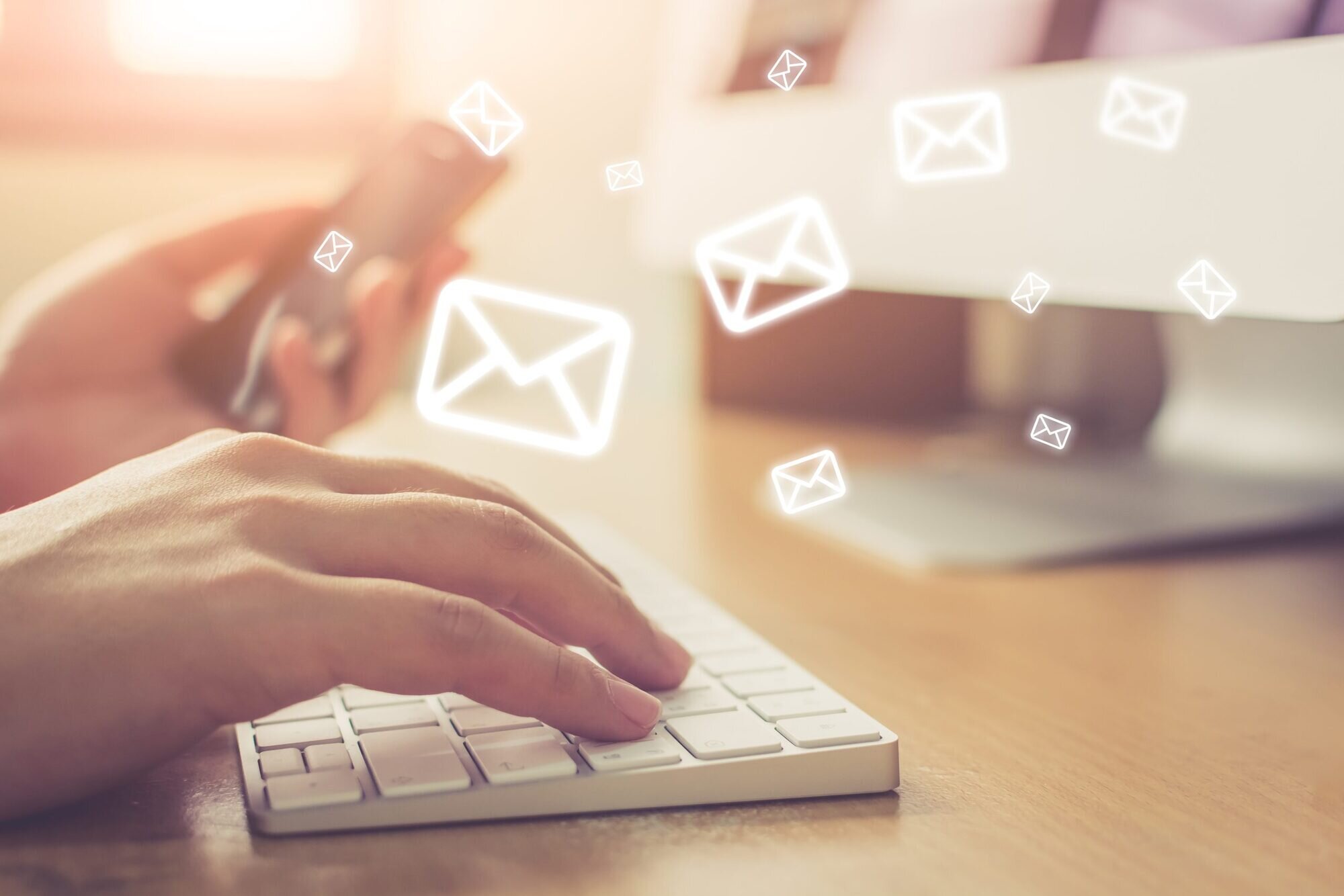 Close-up of hands typing on a keyboard with graphics of envelopes surrounding them