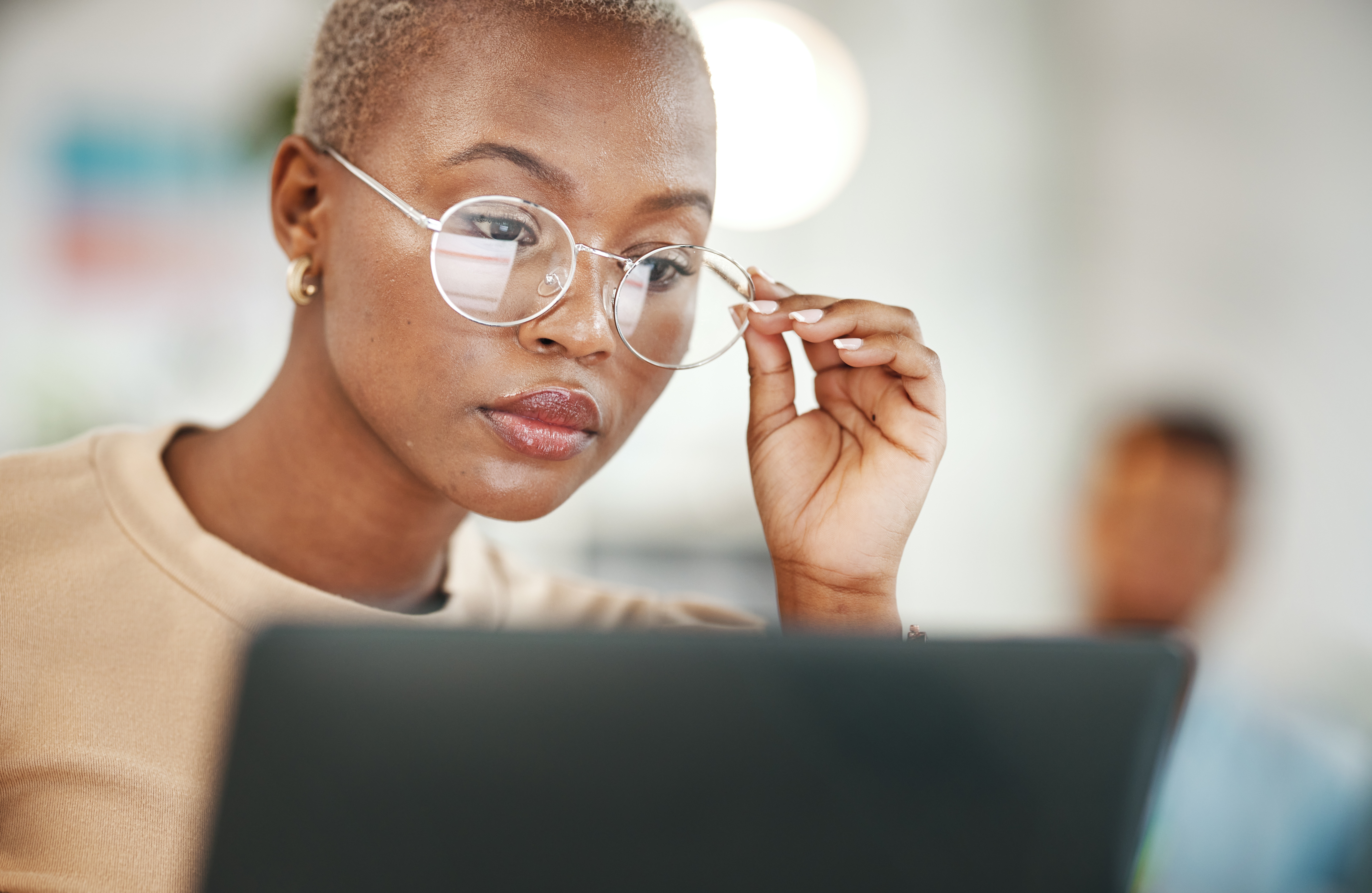 Woman with a hand on her glasses inspecting or reading something closely